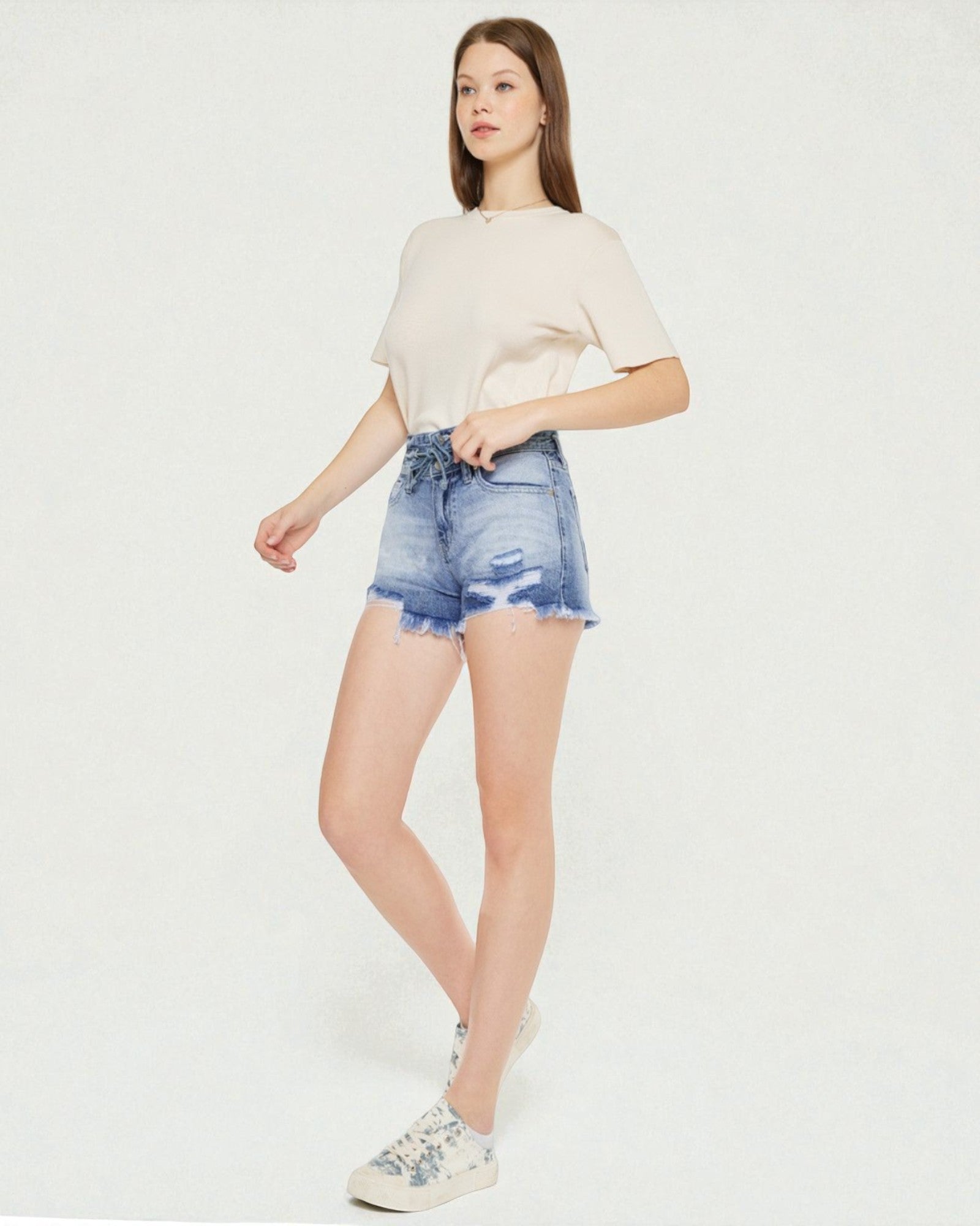 Woman wearing a beige top and blue denim shorts on a white background