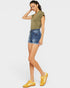 Woman wearing an olive green top and denim shorts with yellow sneakers on a white background