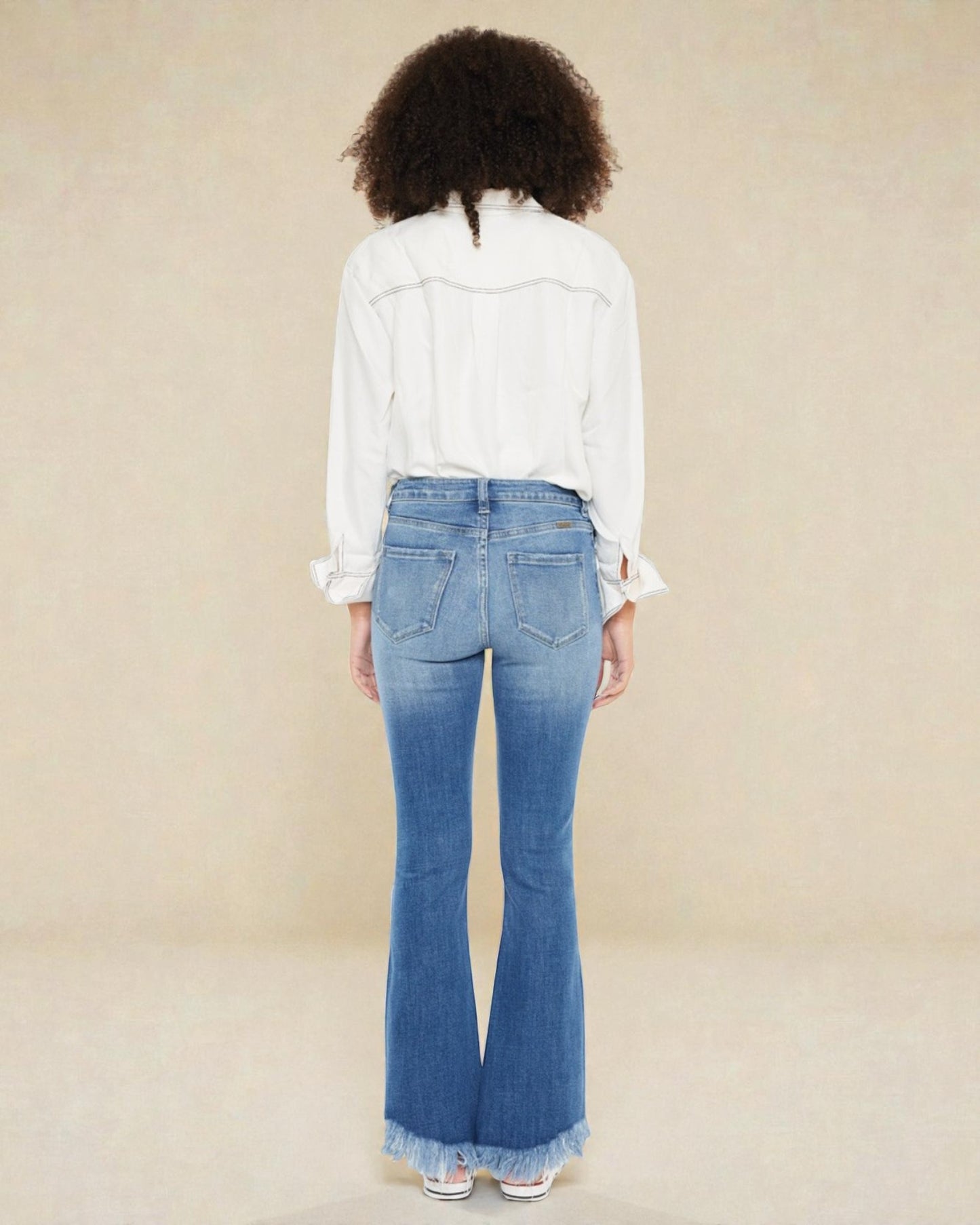 Person wearing blue flared jeans and a white shirt on a beige background
