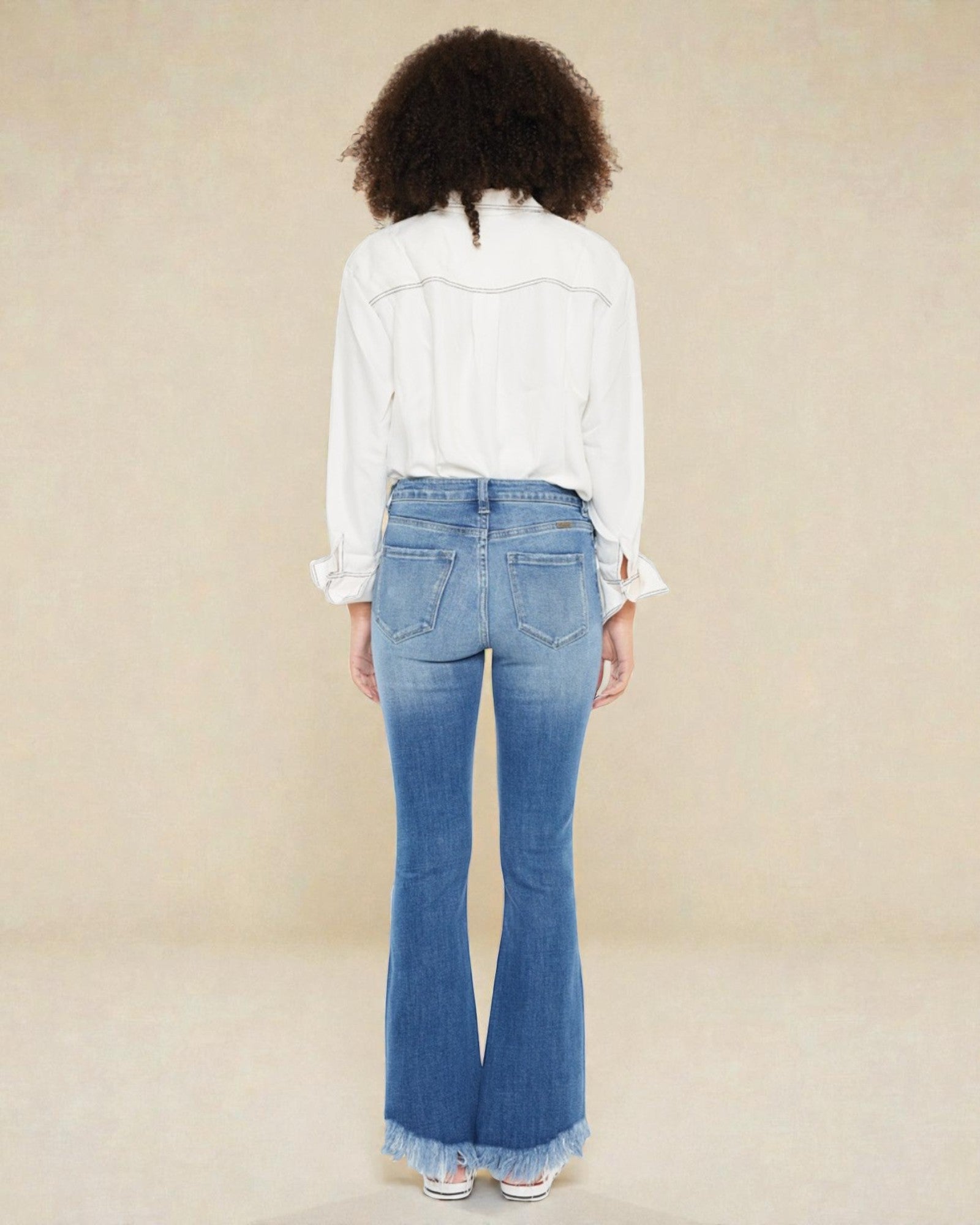 Person wearing blue flared jeans and a white shirt on a beige background
