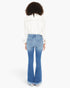 A woman viewed from the back wearing a white long-sleeve blouse and light blue flared jeans with a frayed hem, against a plain white studio background.