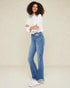 Woman wearing a white blouse and blue jeans against a plain background