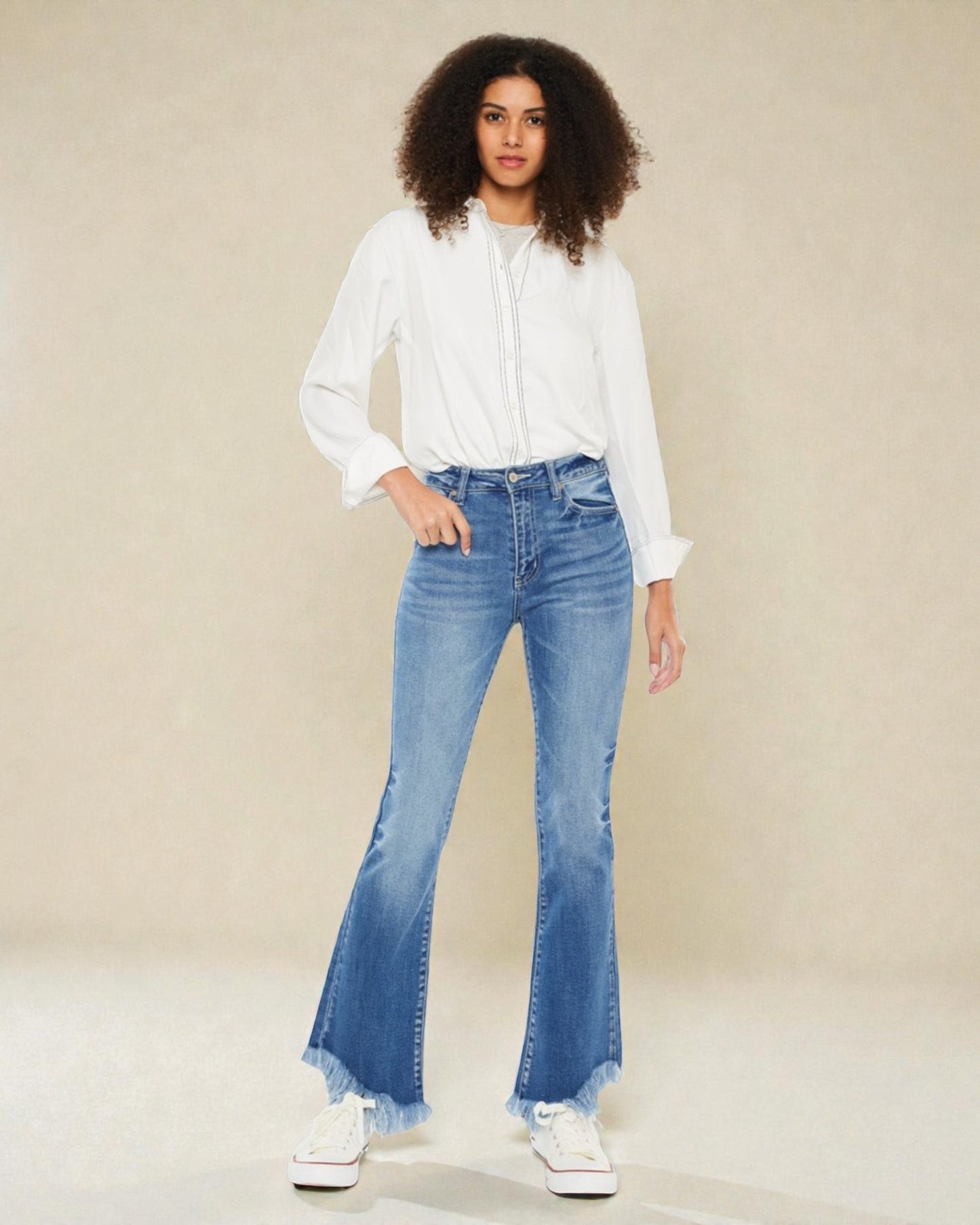 Woman wearing a white blouse and blue flared jeans on a beige background