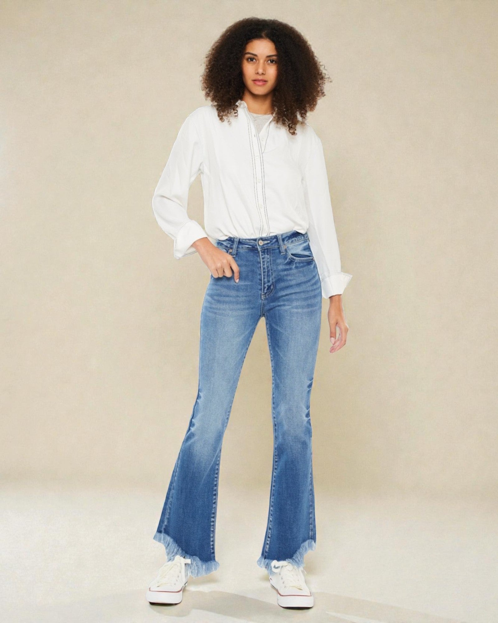 Woman wearing a white blouse and blue flared jeans on a beige background