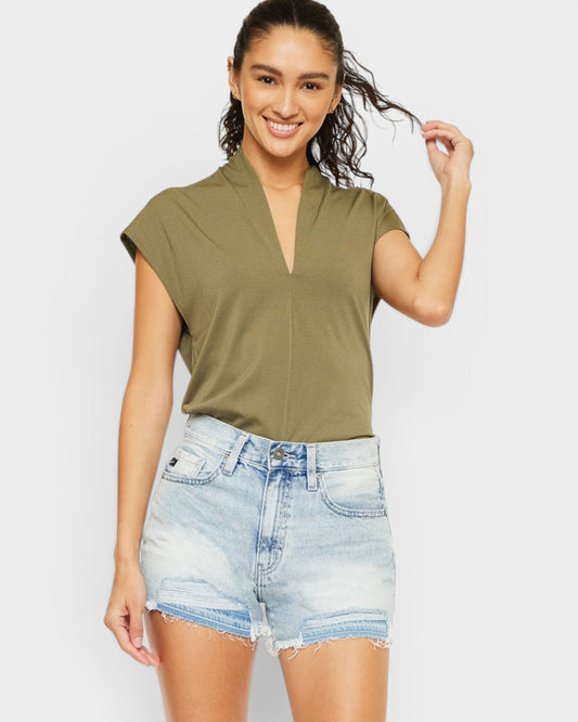 Woman wearing an olive green top and denim shorts on a plain background