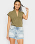 Woman wearing an olive green top and denim shorts on a plain background