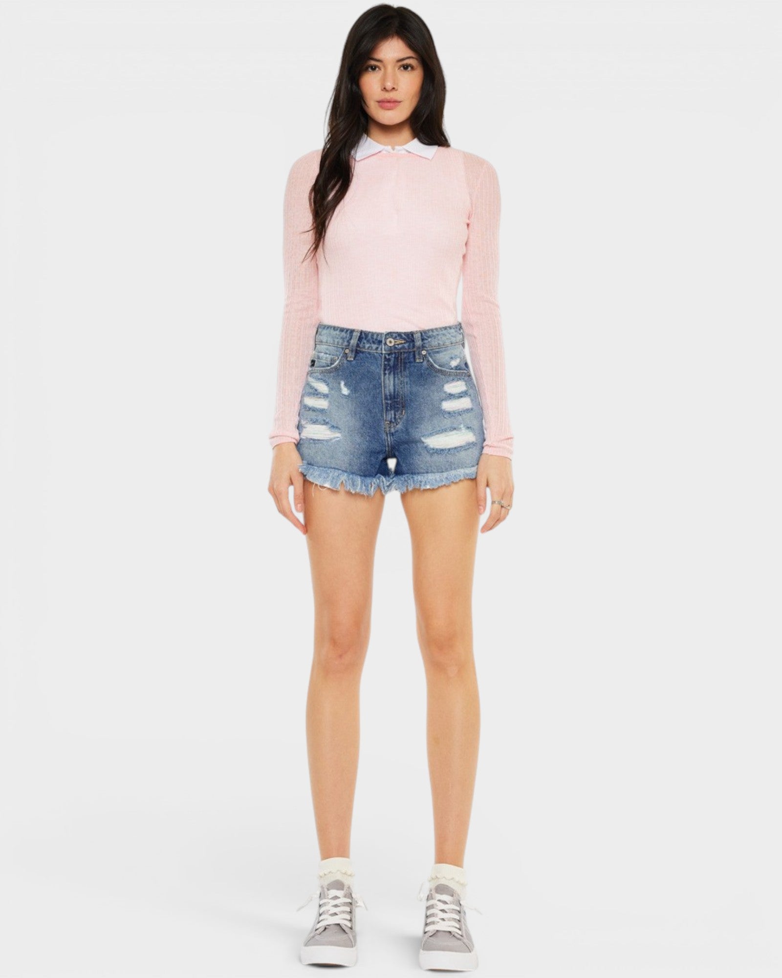 Woman wearing a pink long-sleeve top and denim shorts on a white background