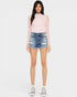 Woman wearing a pink long-sleeve top and denim shorts on a white background