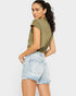 Woman wearing an olive green sleeveless top and light blue denim shorts on a white background