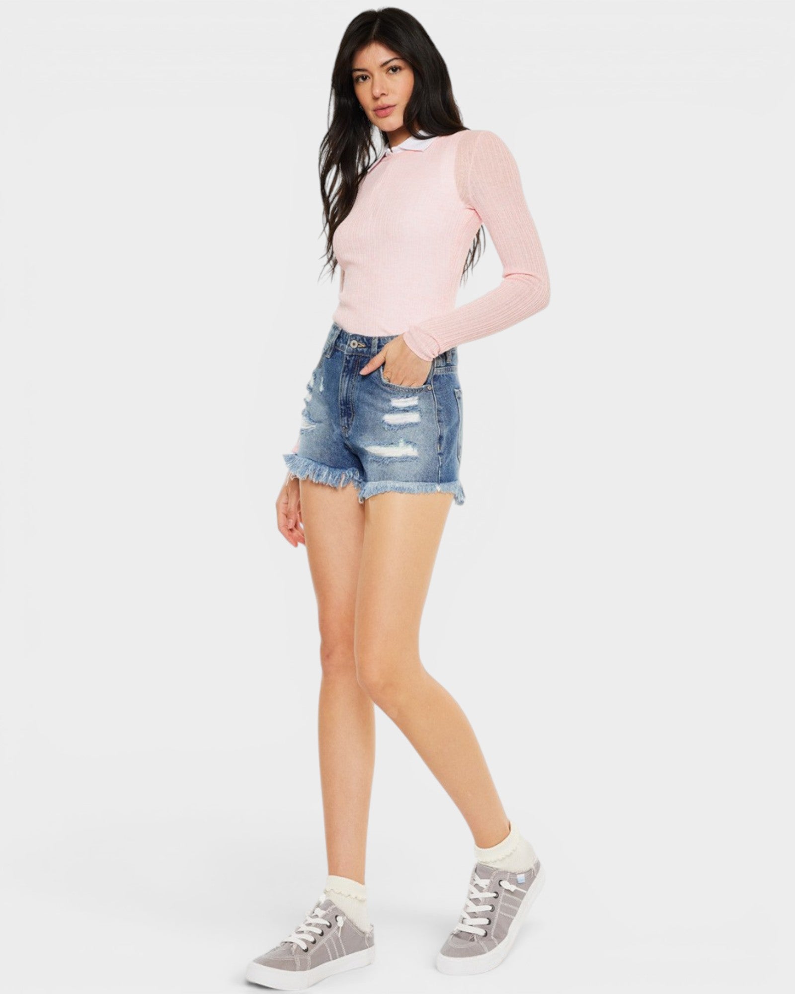 Woman wearing a pink long-sleeve top and denim shorts on a white background