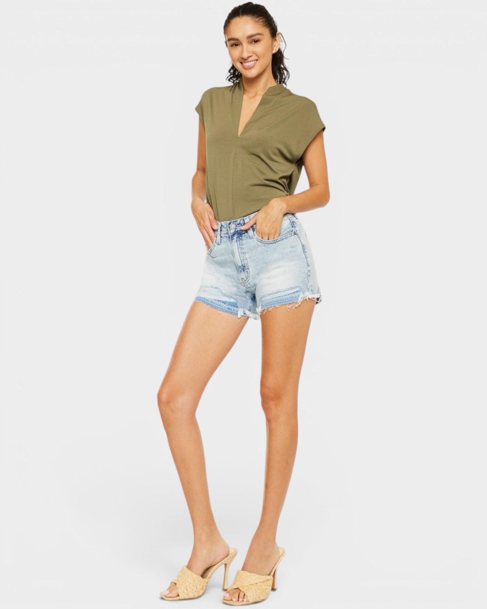 Woman wearing a green top and denim shorts on a white background