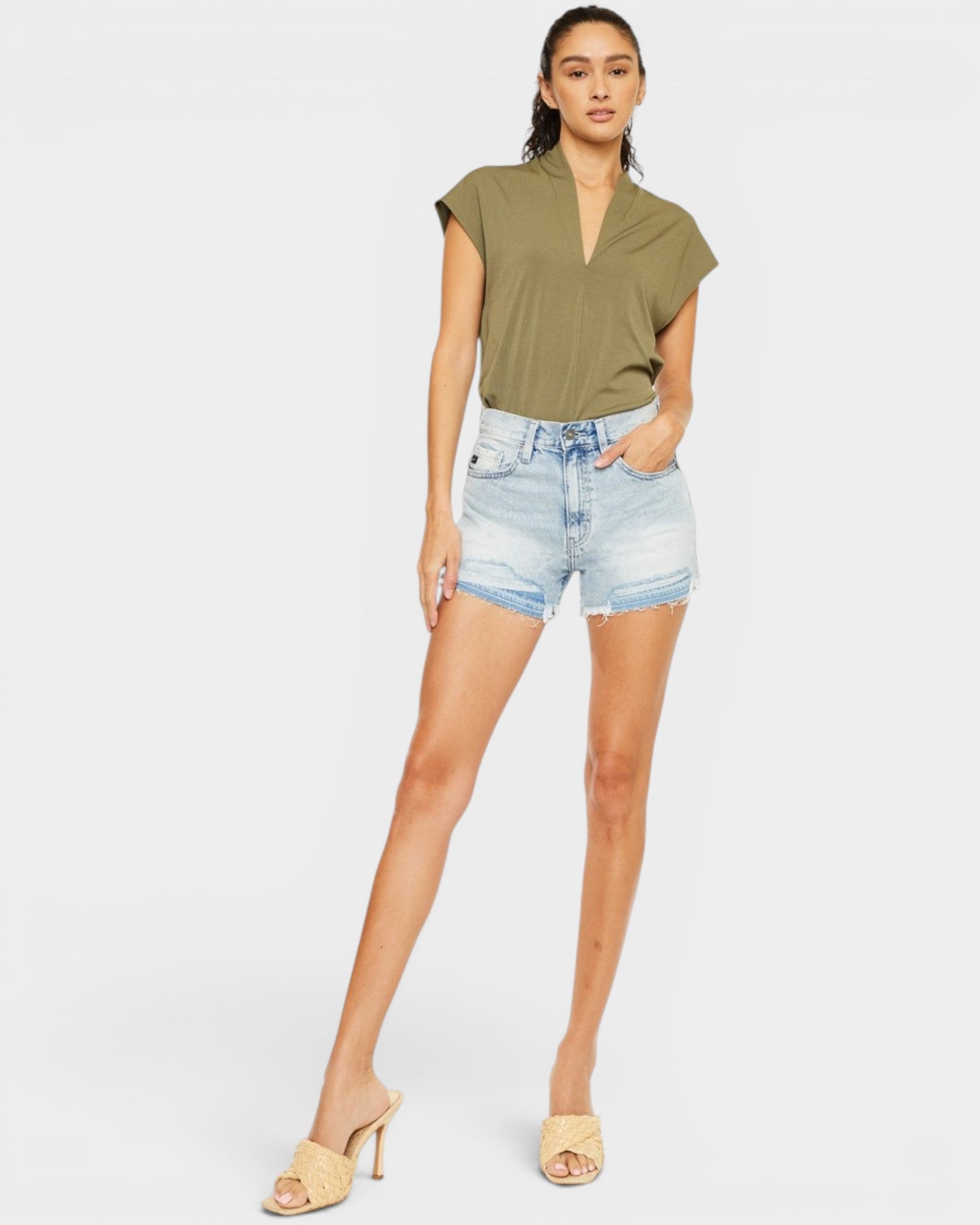 Woman wearing a green top and denim shorts on a white background