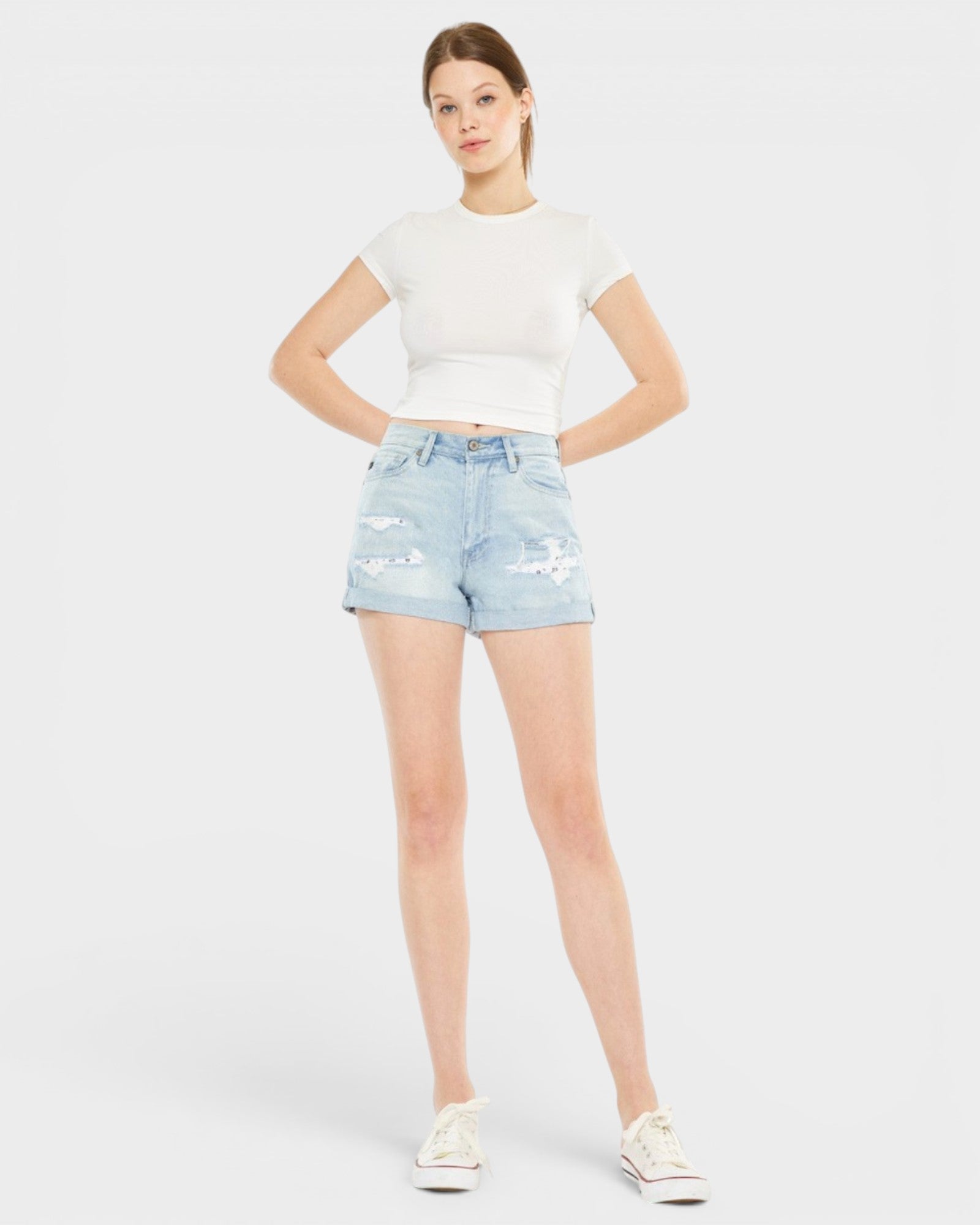 Woman wearing a white t-shirt and light blue denim shorts on a plain background