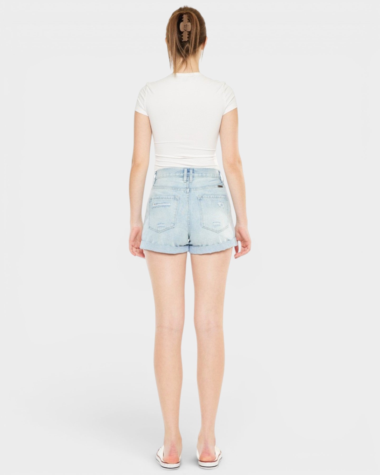 Person wearing light blue denim shorts and a white top on a plain background