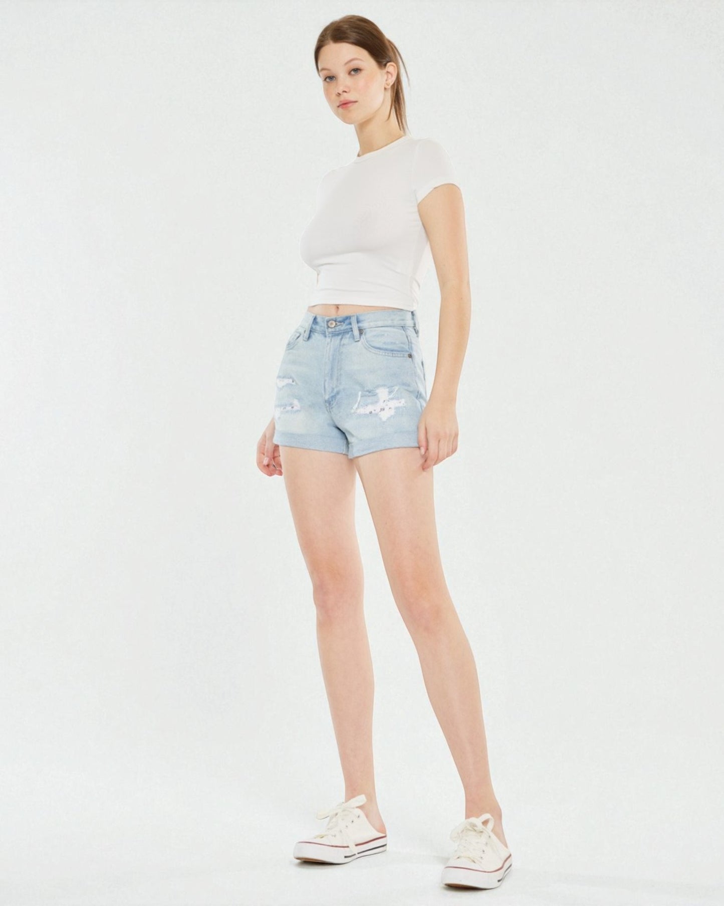 Woman wearing light blue denim shorts and a white t-shirt on a white background