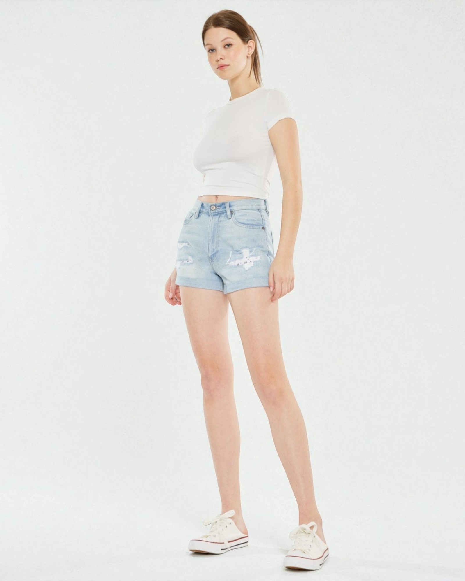 Woman wearing light blue denim shorts and a white t-shirt on a white background