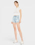 Woman wearing light blue denim shorts and a white top on a plain background