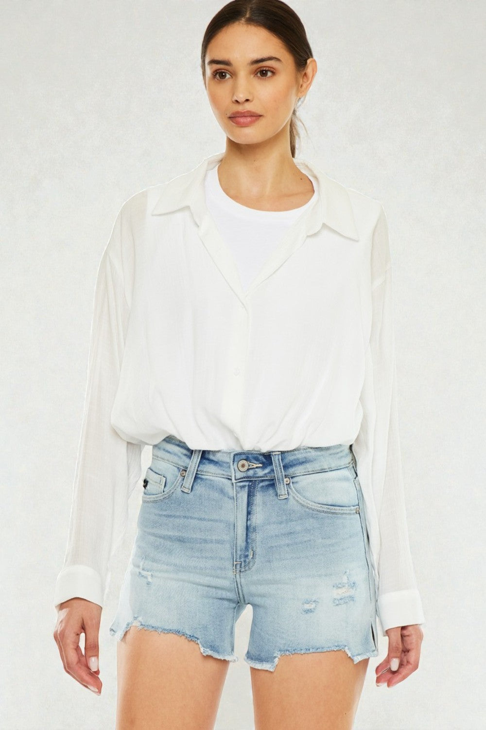 Woman wearing a white blouse and light blue denim shorts on a white background