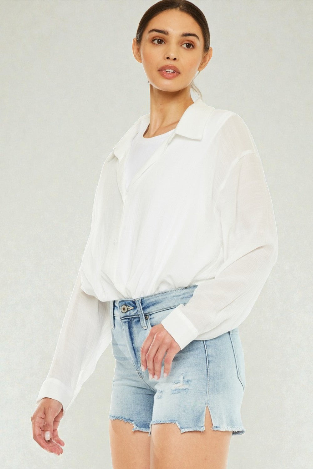 Woman wearing a white shirt and light blue denim shorts on a plain background