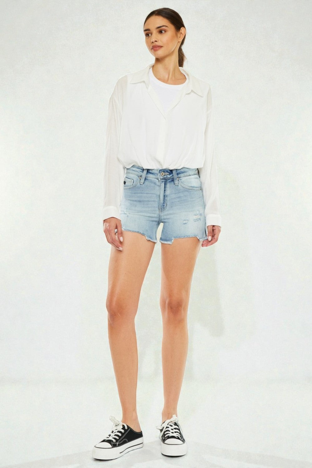 Woman wearing a white jacket, light blue denim shorts, and black sneakers on a white background