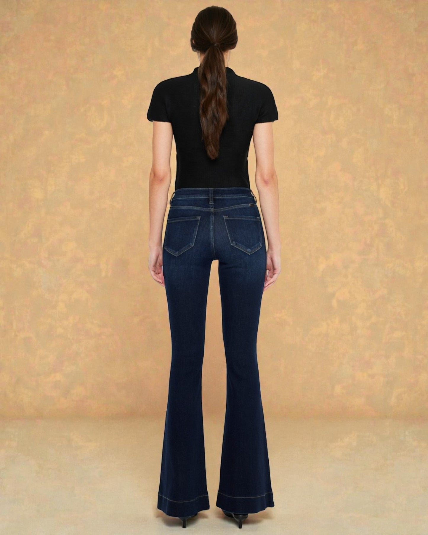 Person wearing dark blue flared jeans and a black top against a beige background