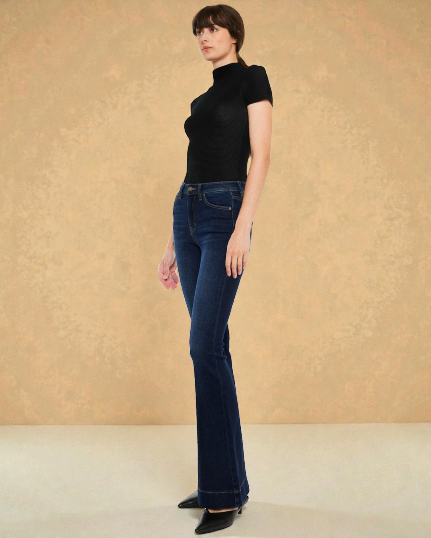 Woman wearing a black top and blue jeans against a beige background