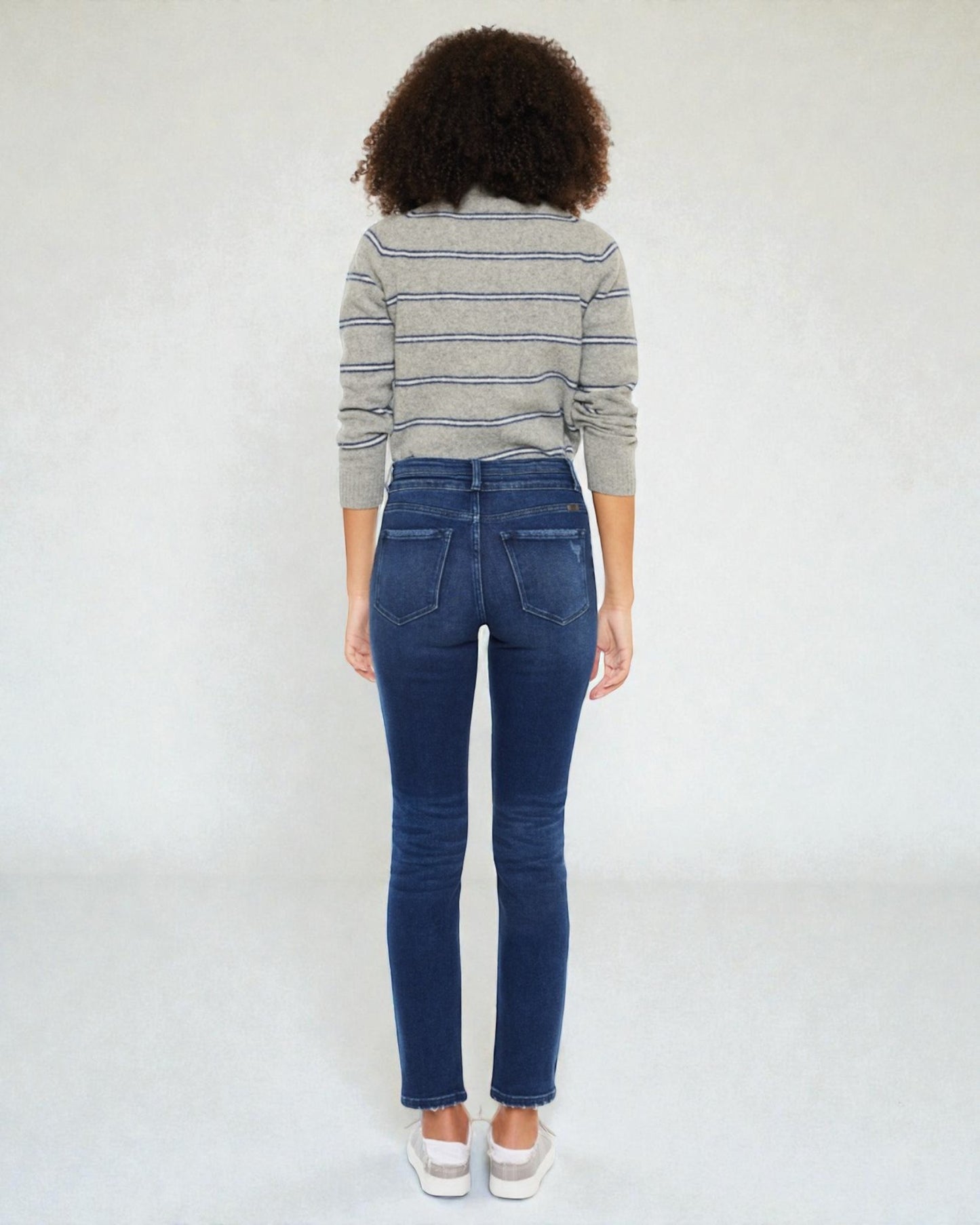 Person wearing a striped sweater and blue jeans against a white background