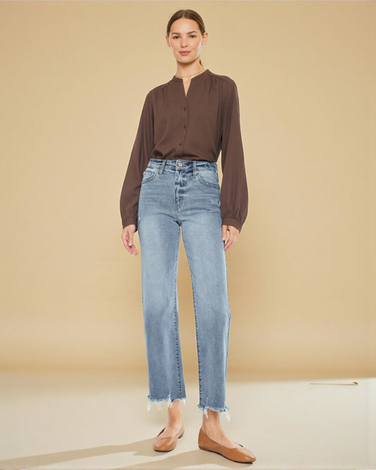 Woman wearing a brown blouse and light blue jeans against a beige background