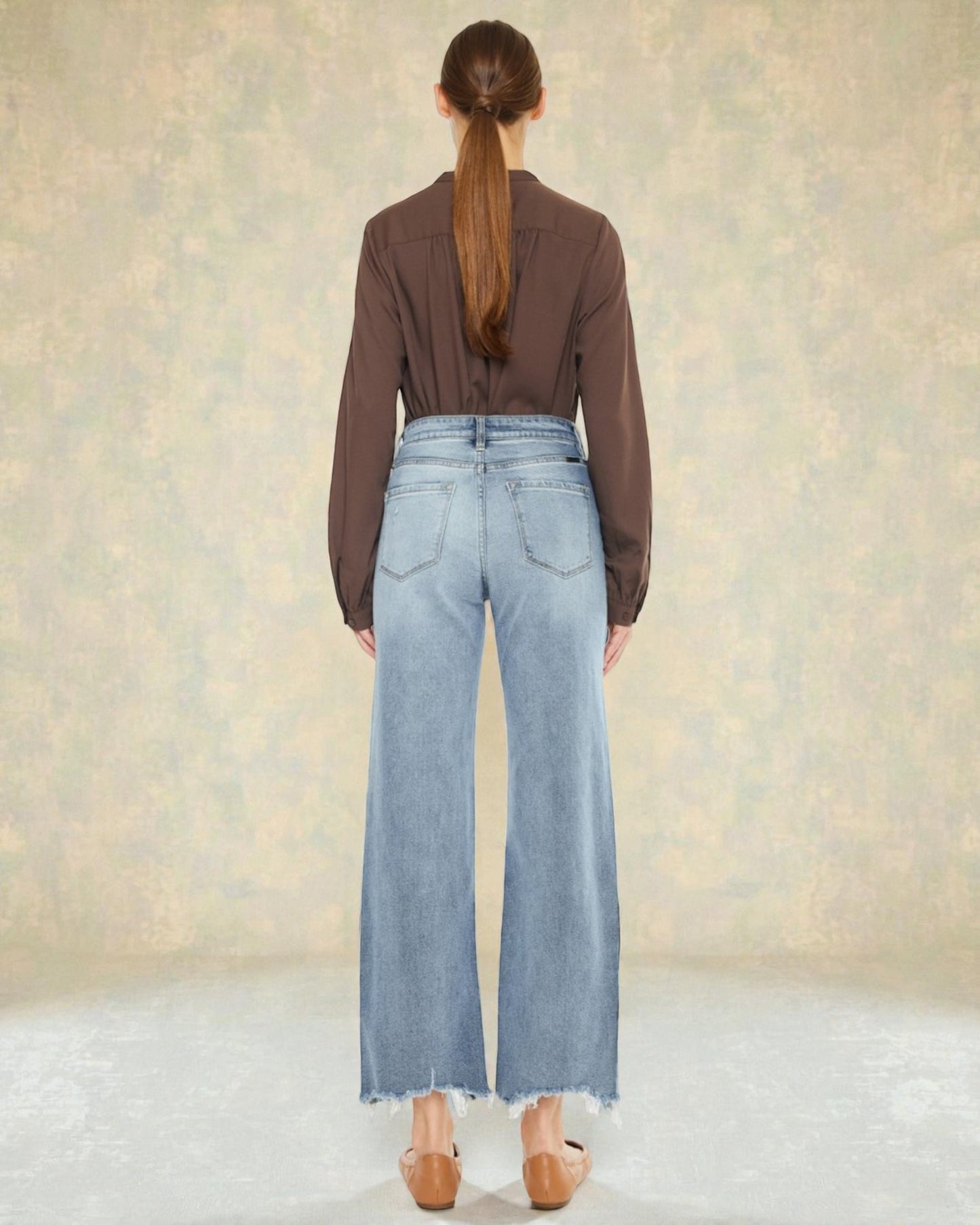 Person wearing a brown shirt and light blue jeans against a neutral background