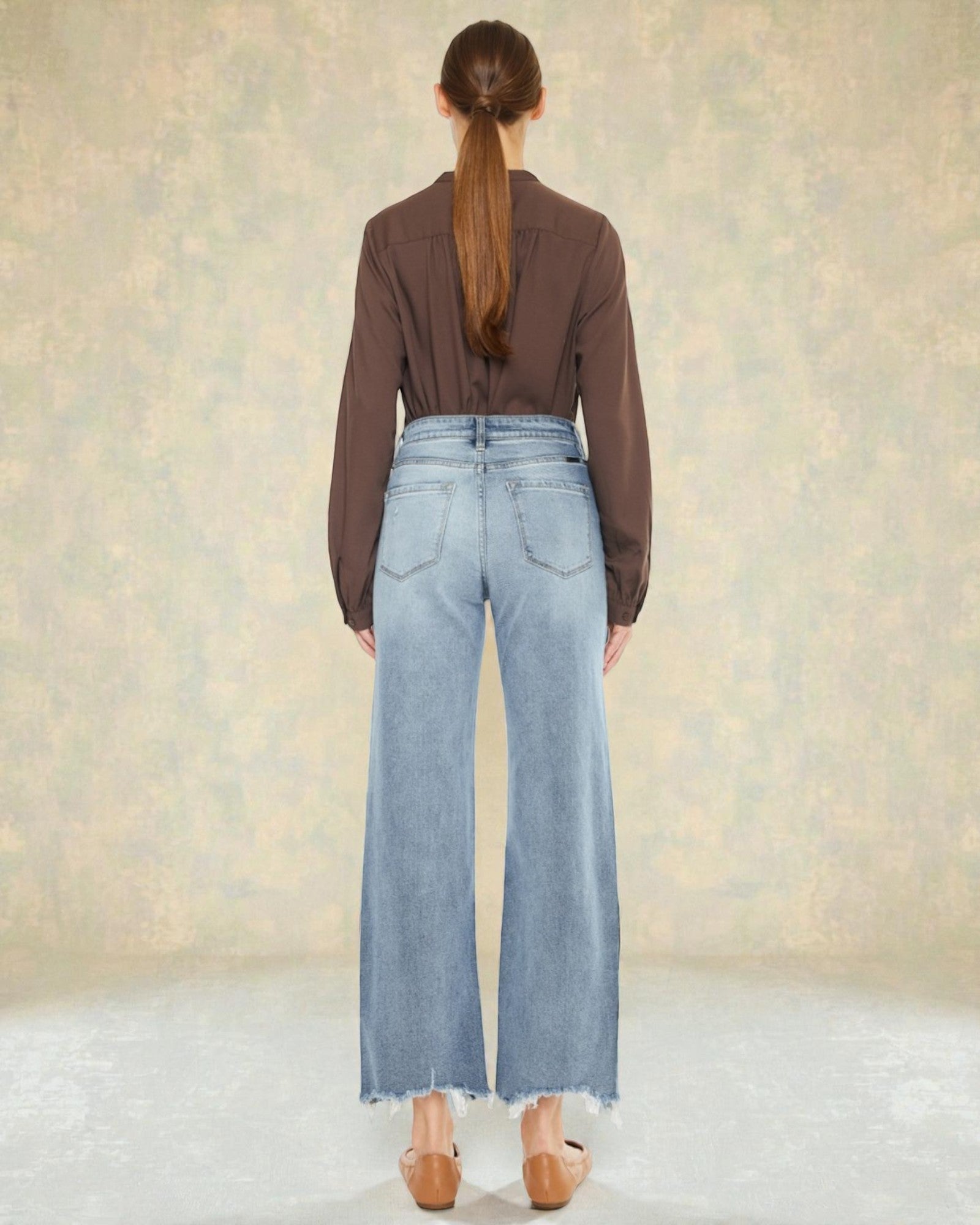 Person wearing a brown shirt and light blue jeans against a neutral background