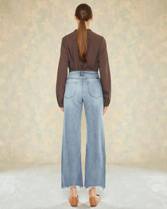 Person wearing a brown shirt and light blue jeans against a neutral background