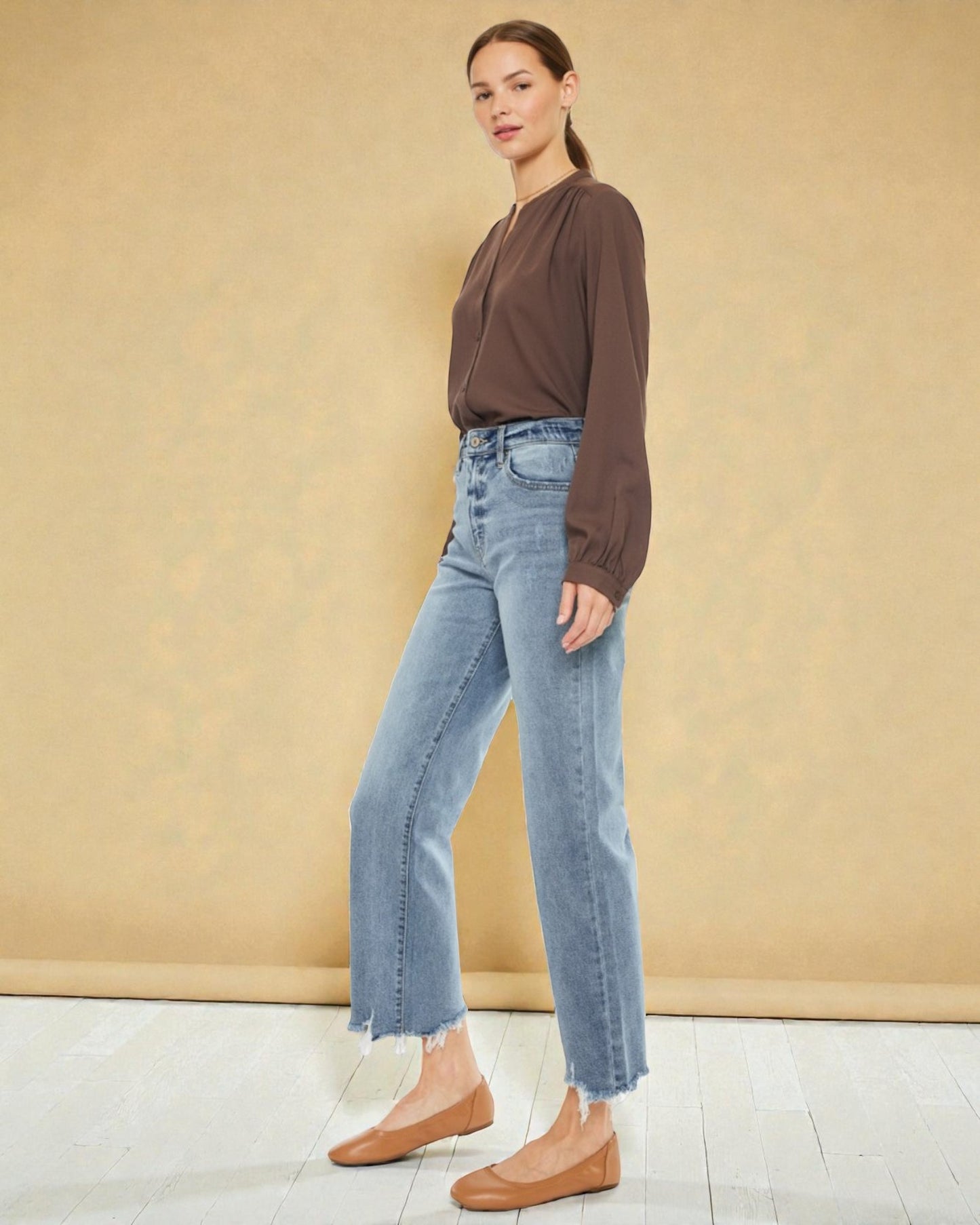 Woman wearing a brown top and light blue jeans against a beige background