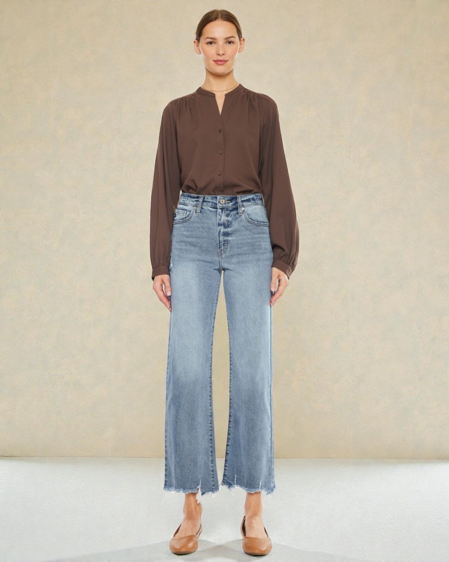 Woman wearing a brown blouse and light blue jeans against a beige background