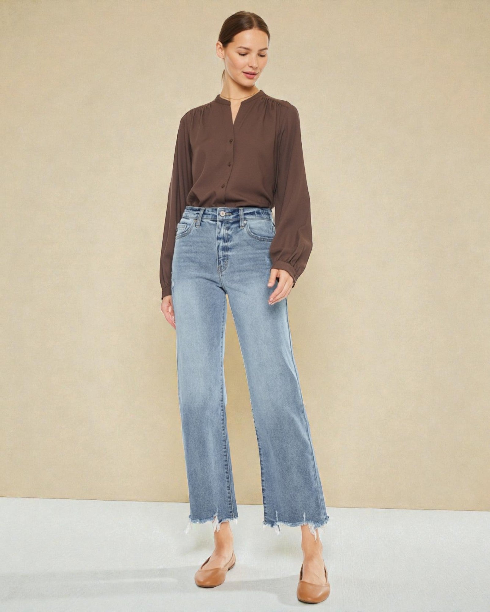 Woman wearing a brown blouse and light blue jeans against a beige background