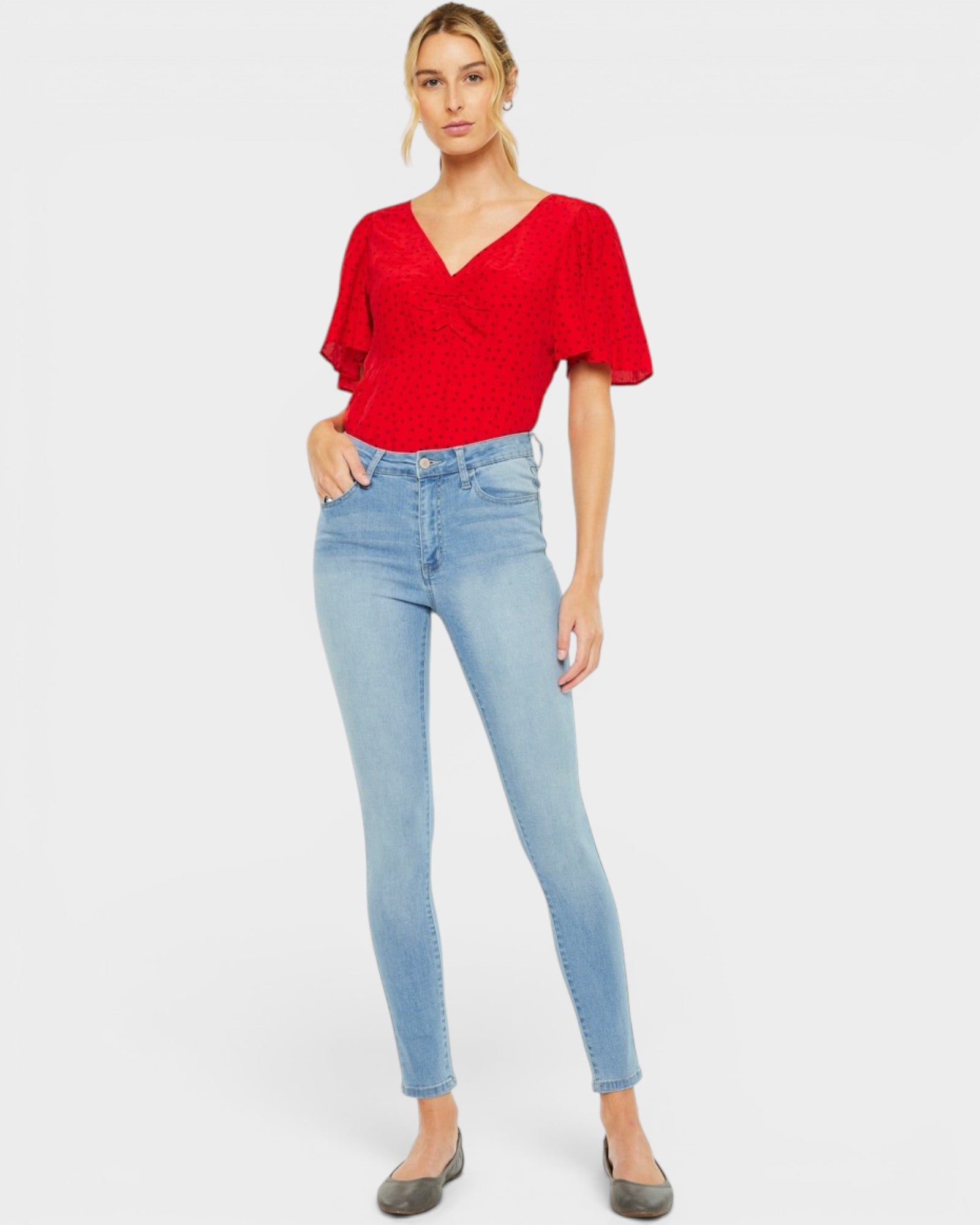 Woman wearing a red top and light blue jeans on a white background