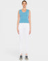 Woman wearing a blue sleeveless top and white pants on a plain background