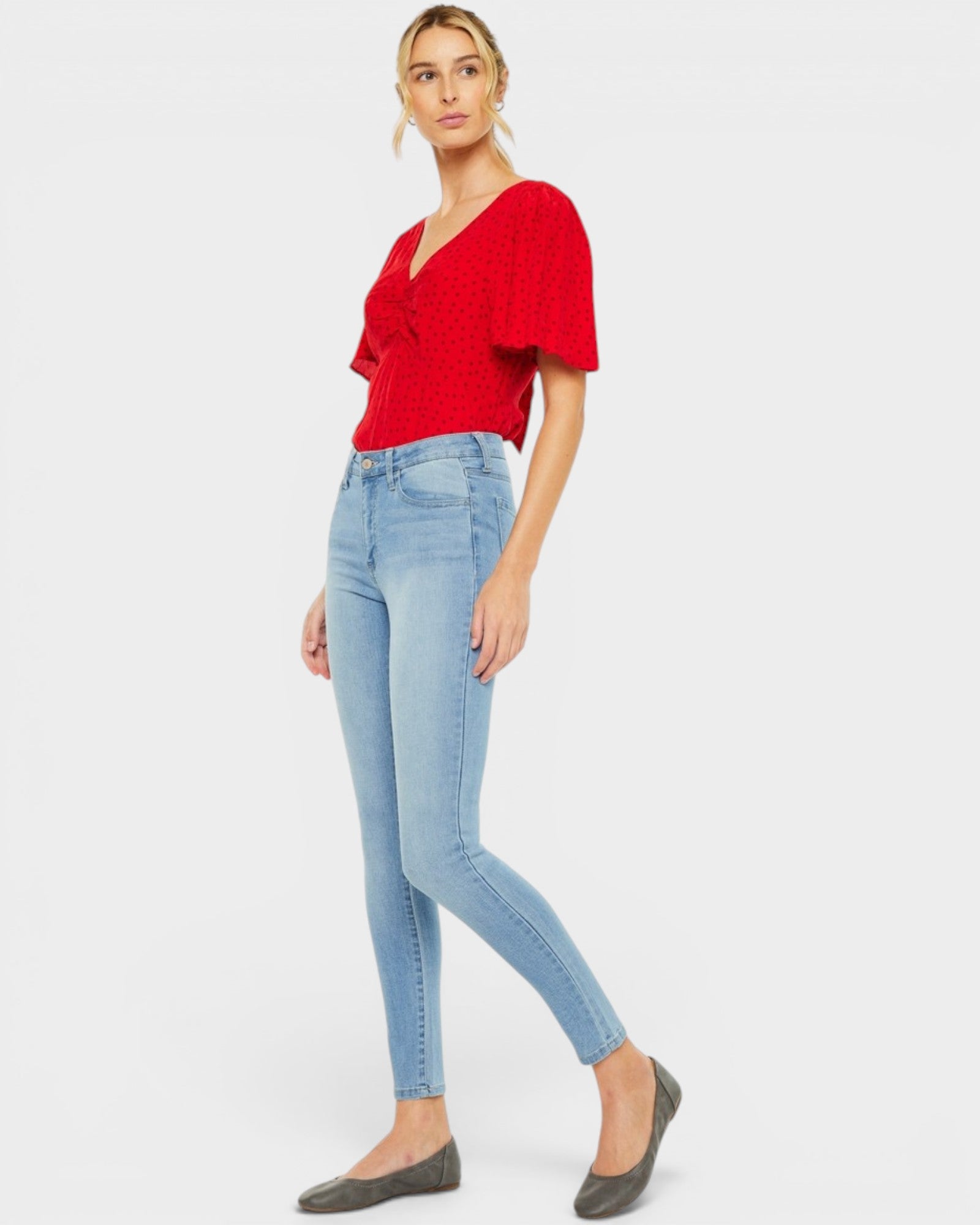Woman wearing a red top and light blue jeans on a white background