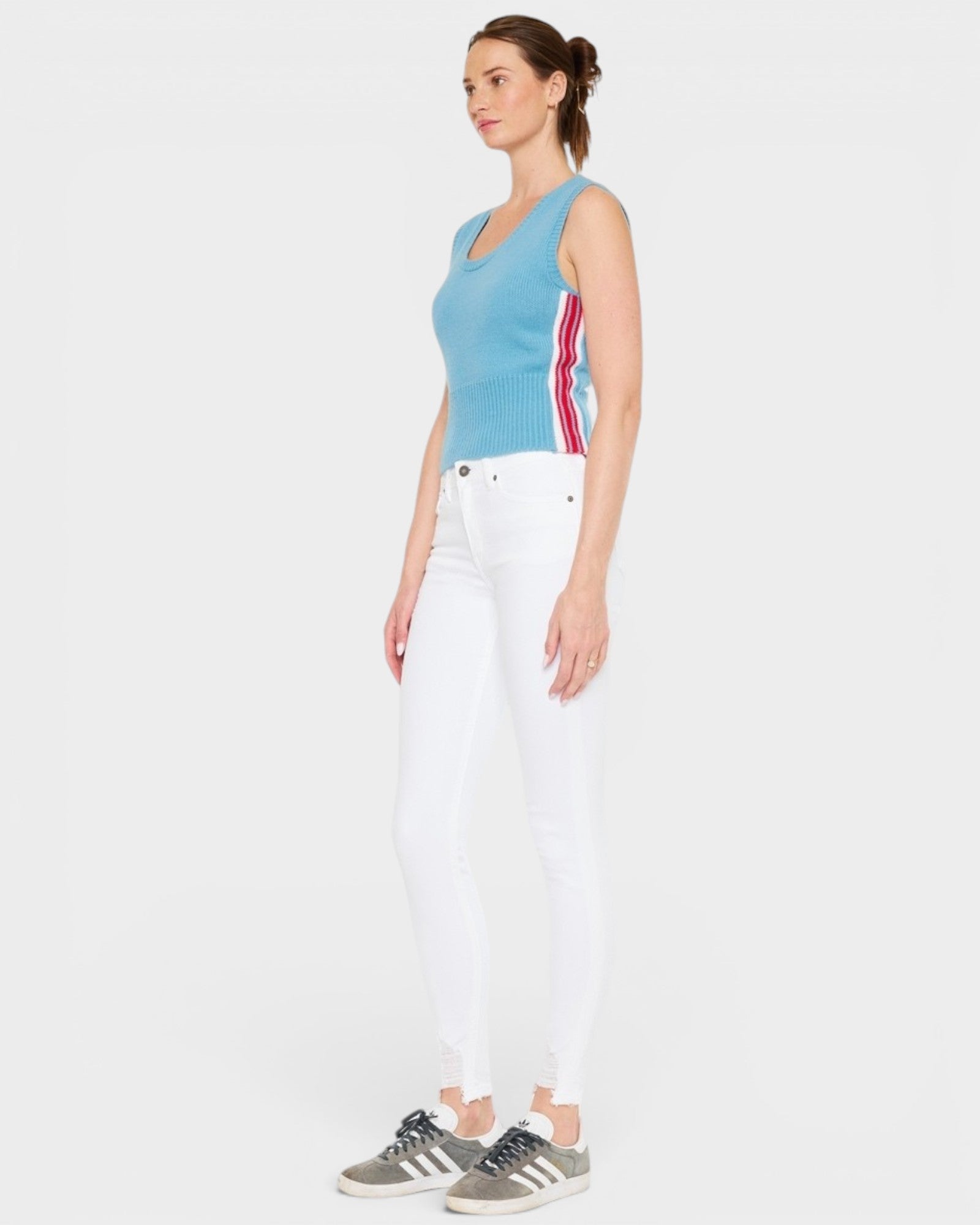 Woman wearing a blue sleeveless top with red and white stripes and white pants on a light gray background