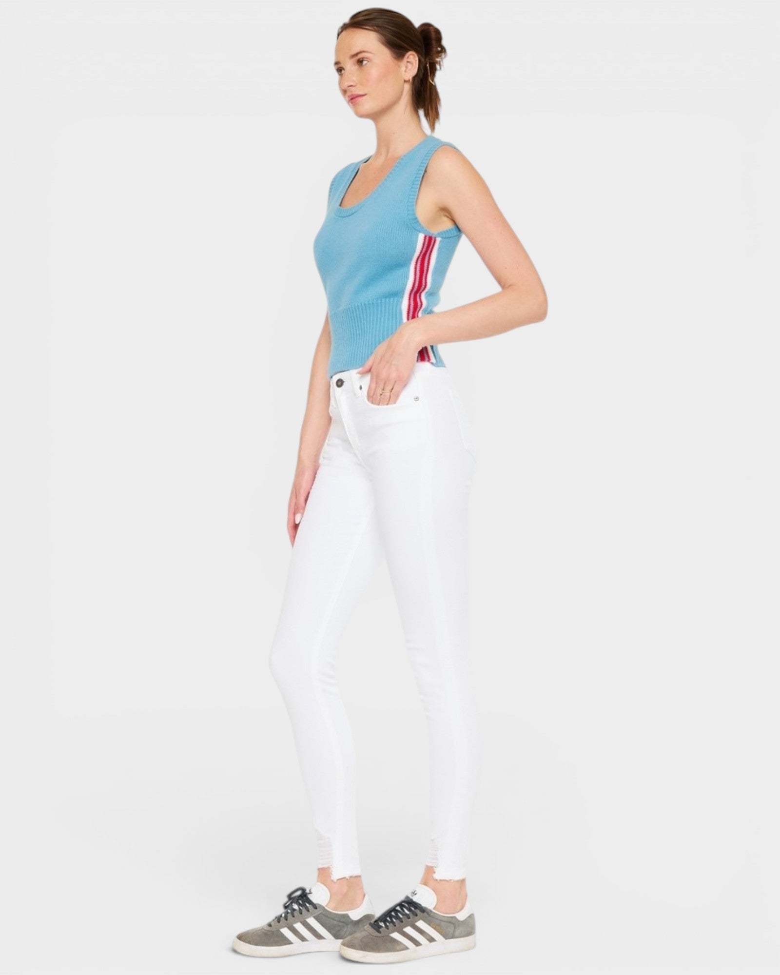 Woman wearing a blue sleeveless top with red stripes and white pants on a light gray background