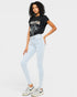 Woman wearing a black t-shirt with graphic design, light blue jeans, and white sneakers on a plain background