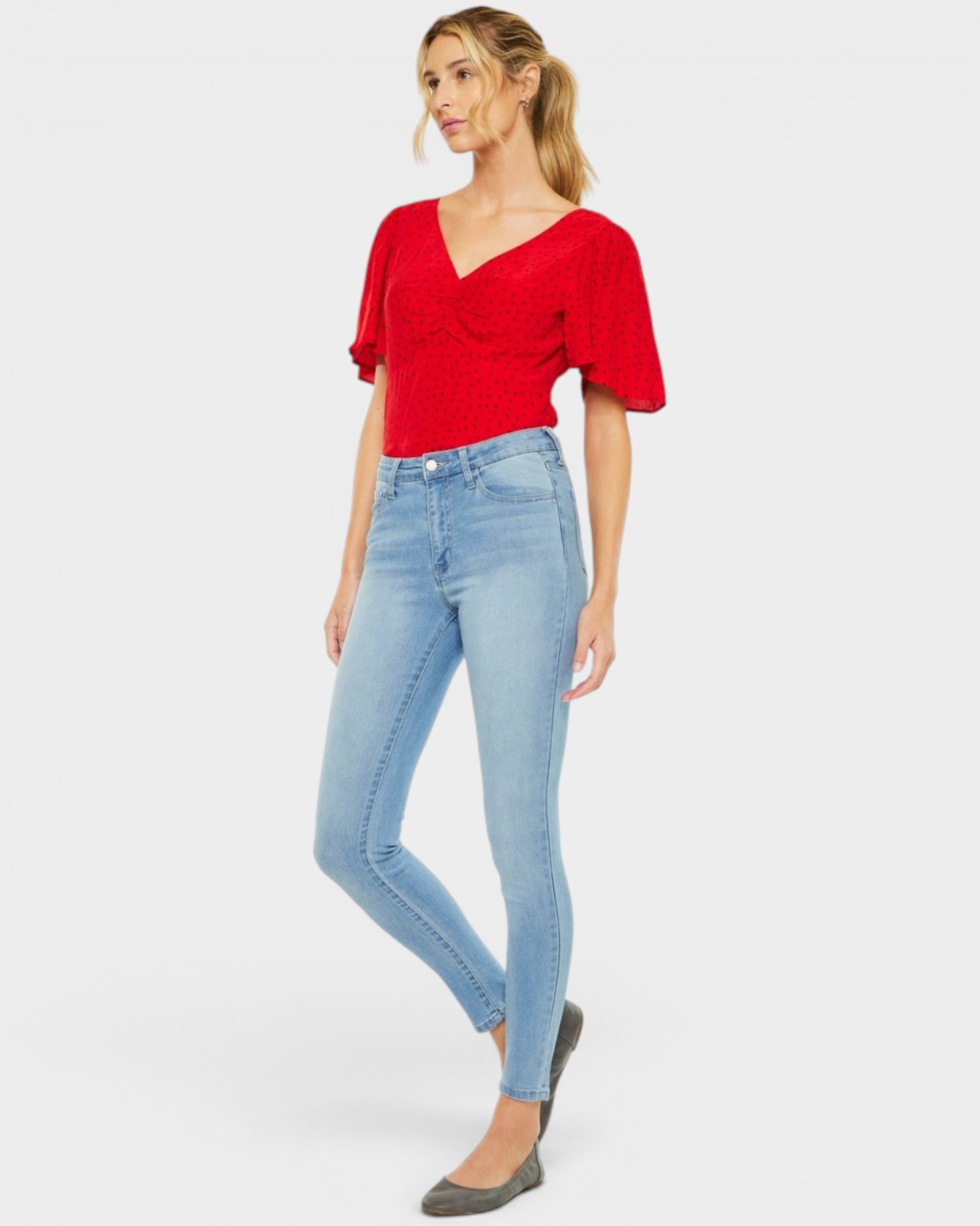 Woman wearing a red top and light blue jeans on a white background