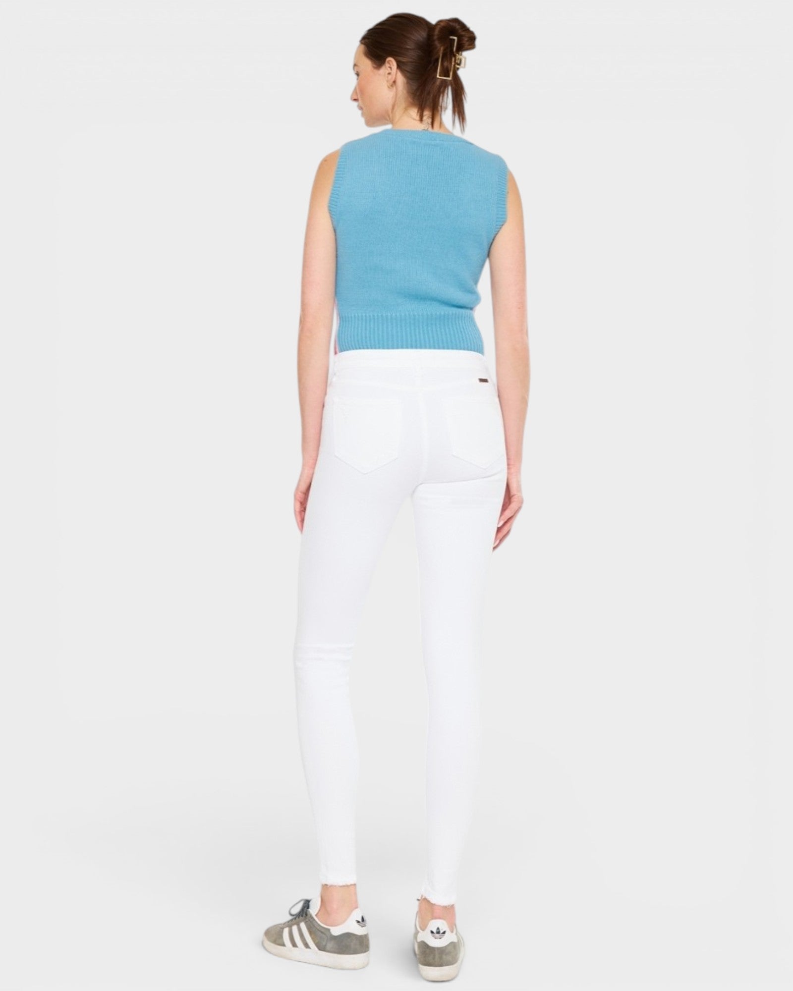 Woman wearing a blue sleeveless top and white pants on a plain background