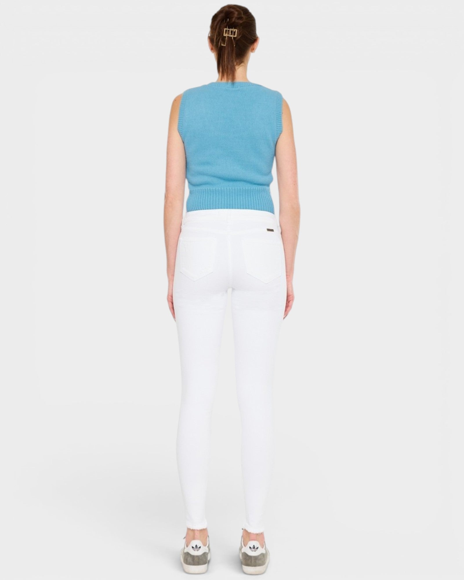 Person wearing a blue sleeveless top and white pants on a light gray background