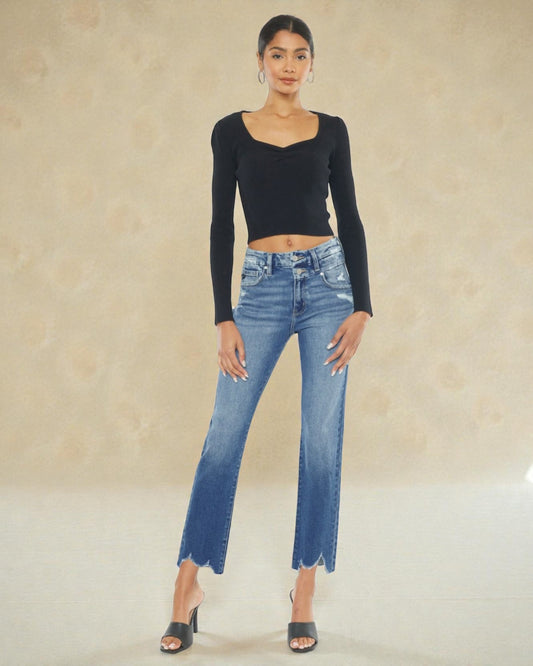 Woman wearing a black long-sleeve top and blue jeans against a beige background