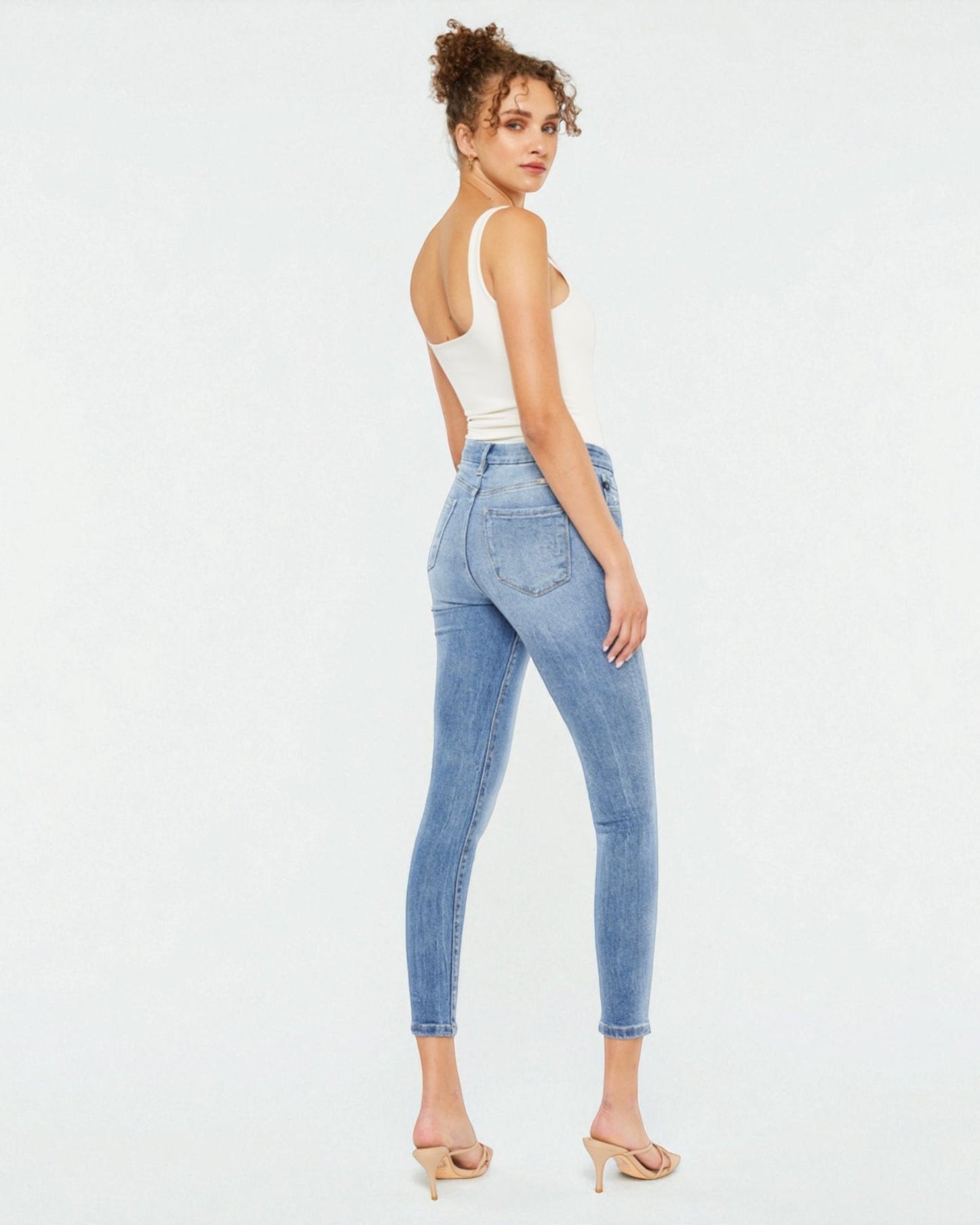 Woman wearing light blue jeans and a white top on a white background