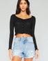 Woman wearing a black long-sleeve crop top and denim shorts on a plain background