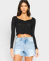 Woman wearing a black long-sleeve crop top and denim shorts on a plain background