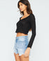 Woman wearing a black long-sleeve crop top and light blue denim shorts on a white background