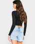 Woman wearing a black long-sleeve top and denim shorts on a plain background