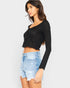 Woman wearing a black long-sleeve crop top and light blue denim shorts on a white background